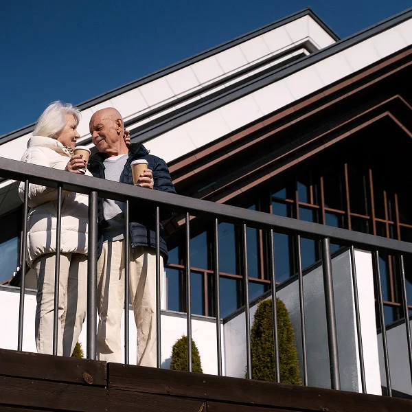 Un couple âgé se tenant sur un balcon, souriant et profitant de la vue ensemble.